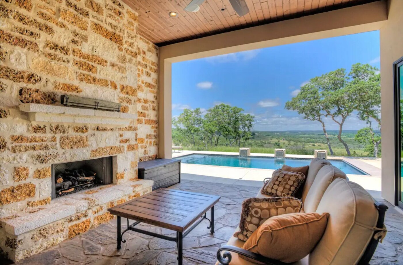 Covered patio with a stone fireplace, pool and valley views